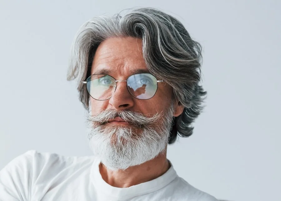 Sits on the sofa. Senior stylish modern man with grey hair and beard indoors