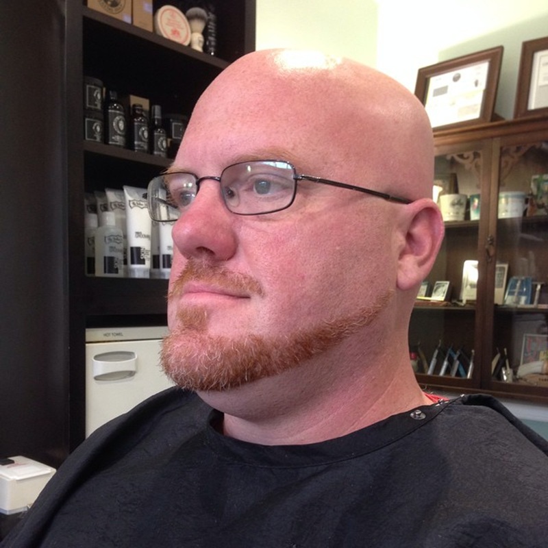 A red anchor beard featuring a pointed goatee and a disconnected mustache on a man with a round face