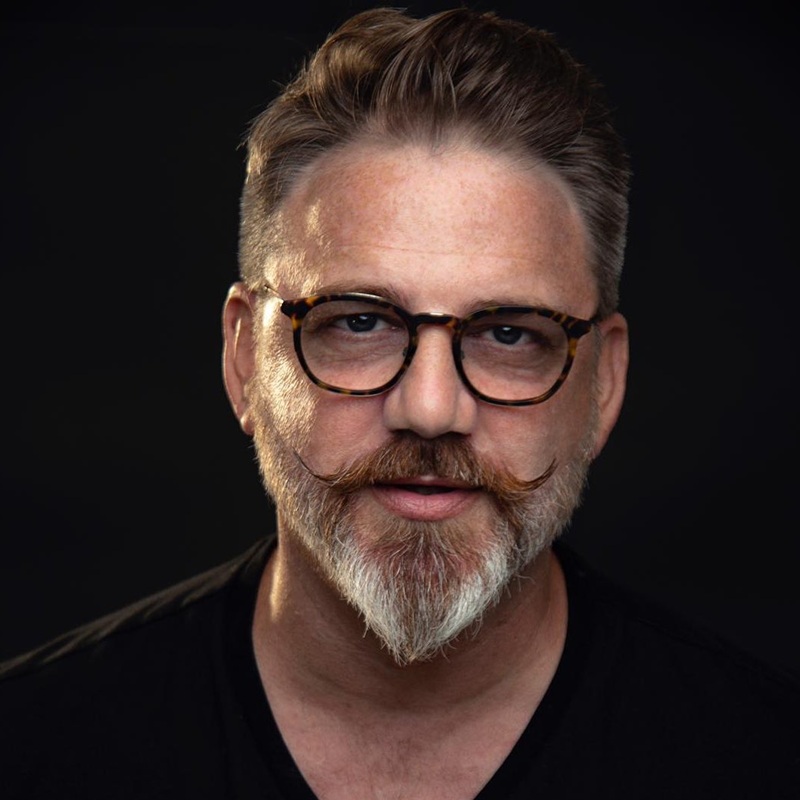well-groomed ducktail beard styled into a sharp, pointed chin with a handlebar mustache on a round face