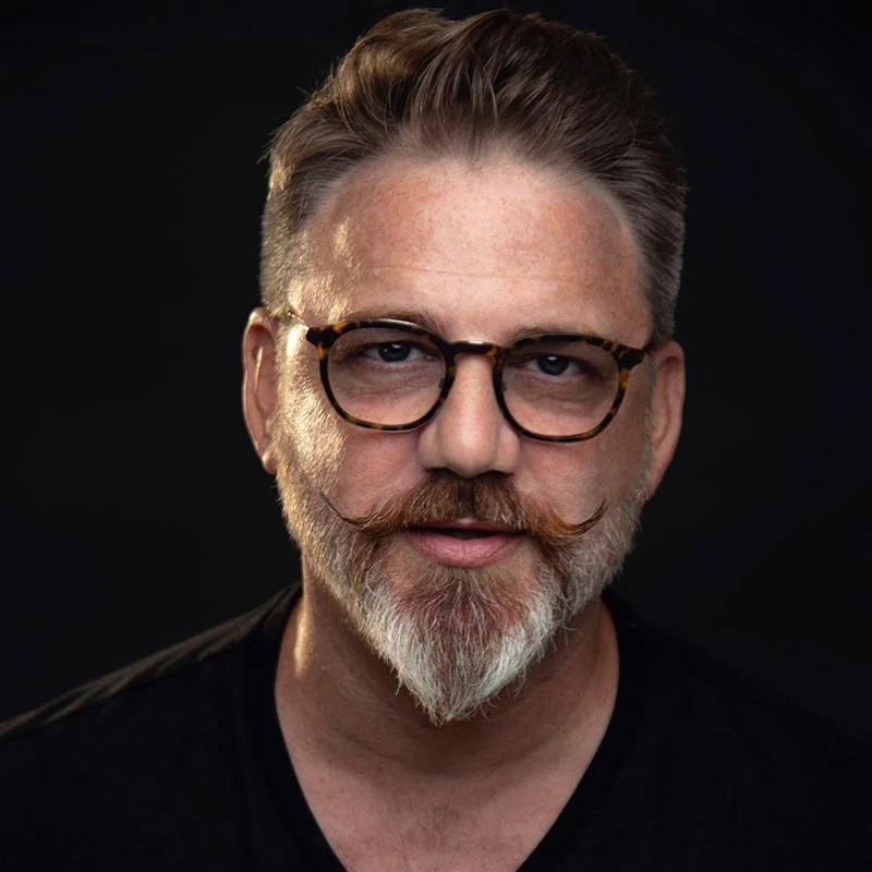 well-groomed ducktail beard styled into a sharp, pointed chin with a handlebar mustache on a round face